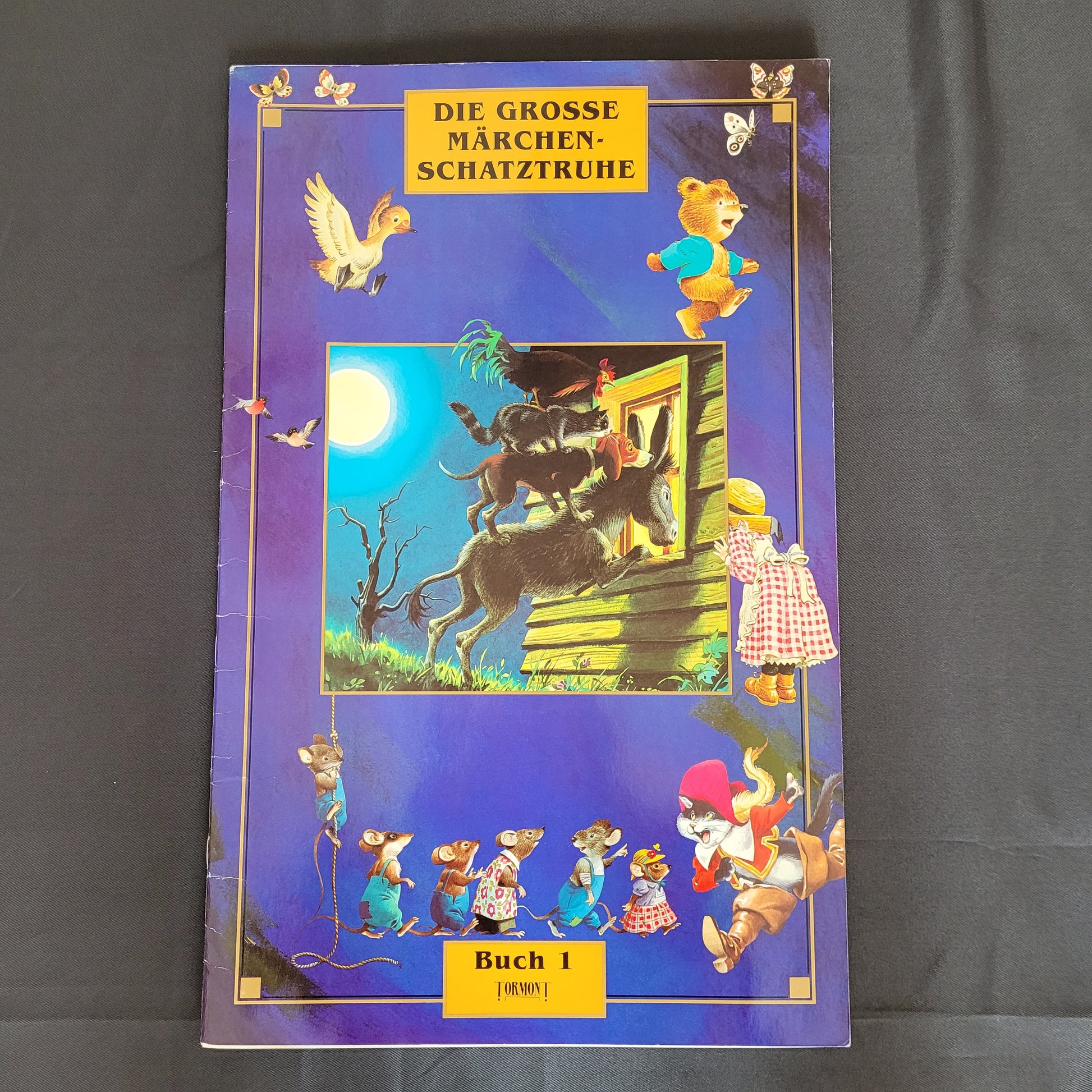 Vintage Cover des Kinderbuchs „Die große Märchenschatztruhe – Buch I“ mit liebevoll gestalteten Illustrationen klassischer Märchenfiguren wie der Wolf und die sieben Geißlein, Bären mit Honigtopf und Mäusen in Kleidung auf dunkelblauem Hintergrund. Das nostalgische Design macht dieses Vintage-Märchenbuch zu einem charmanten Sammlerstück für Liebhaber traditioneller Kinderliteratur und Märchenklassiker.