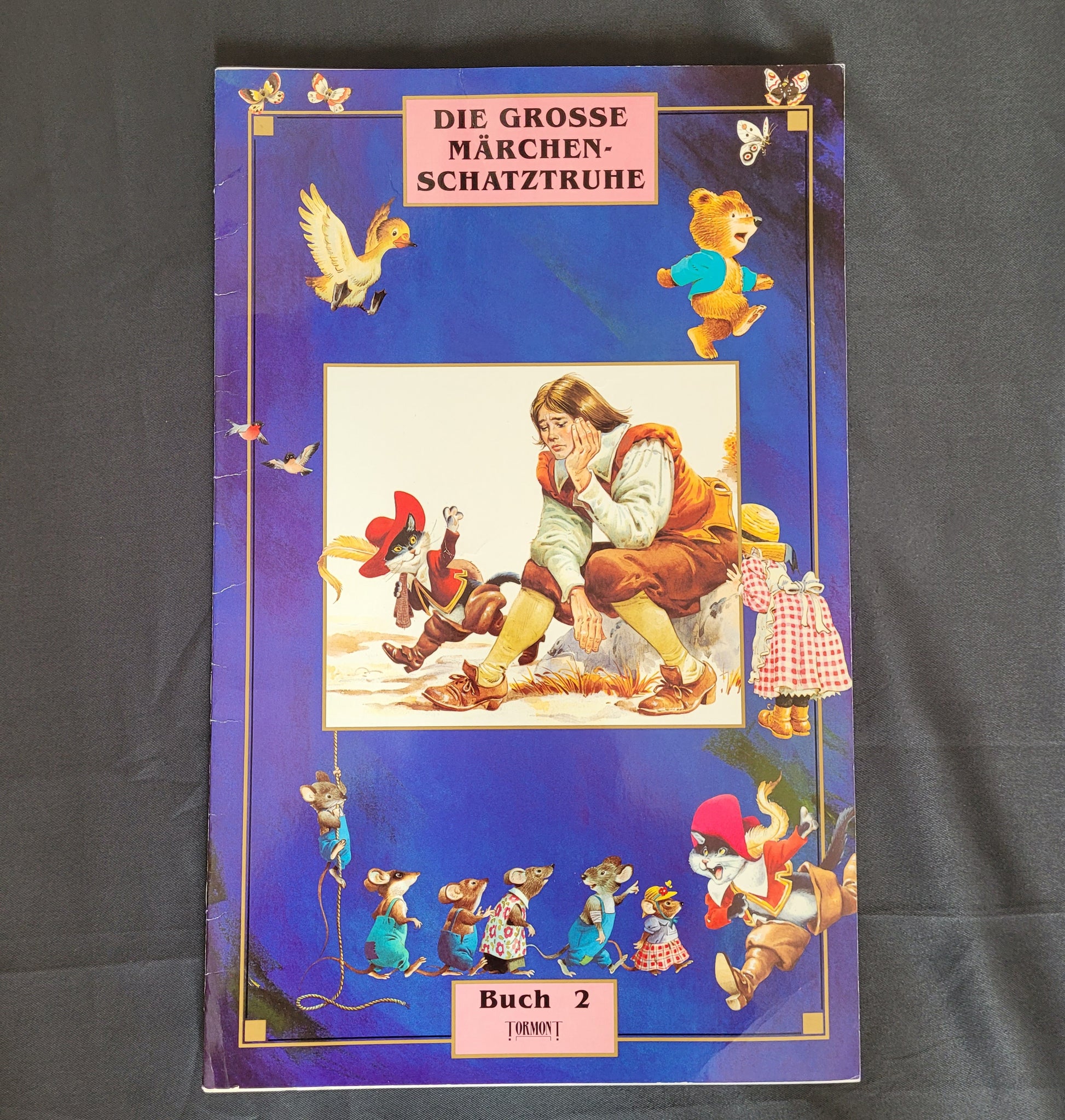Vintage Cover des Märchenbuchs „Die große Märchenschatztruhe – Buch 2“ mit farbenfrohen Illustrationen klassischer Märchenfiguren wie Zwerge, Tiere in Kleidung und fantasievollen Szenen auf tiefblauem Hintergrund. Das nostalgische Design und die liebevolle Gestaltung machen dieses Vintage-Märchenbuch zu einem begehrten Sammlerstück für Märchenfreunde und Liebhaber traditioneller Kinderliteratur.