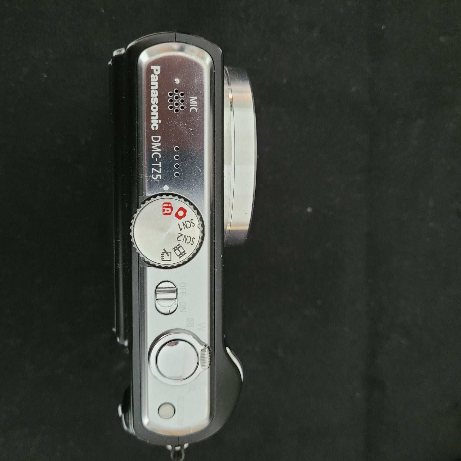 Draufansicht der Panasonic Lumix DMC-TZ5 Digitalkamera liegt auf einem schwarzen Untergrund. Es sind verschiedene Bezeichnungen zu lesen wie MIC oder DMC-TZ5.