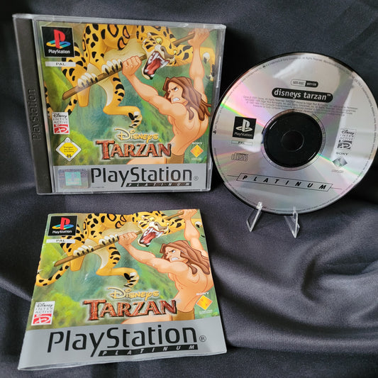 PlayStation 1 Spiel Disney’s Tarzan mit Original-CD, Spielehülle und Anleitung. Die CD trägt den Titel Disney’s Tarzan mit PlayStation-Logo. Auf Hülle und Anleitung ist Tarzan abgebildet, wie er an einer Liane schwingt, während ein Leopard angreift. PlayStation-Branding und Disney-Logo sind deutlich sichtbar.