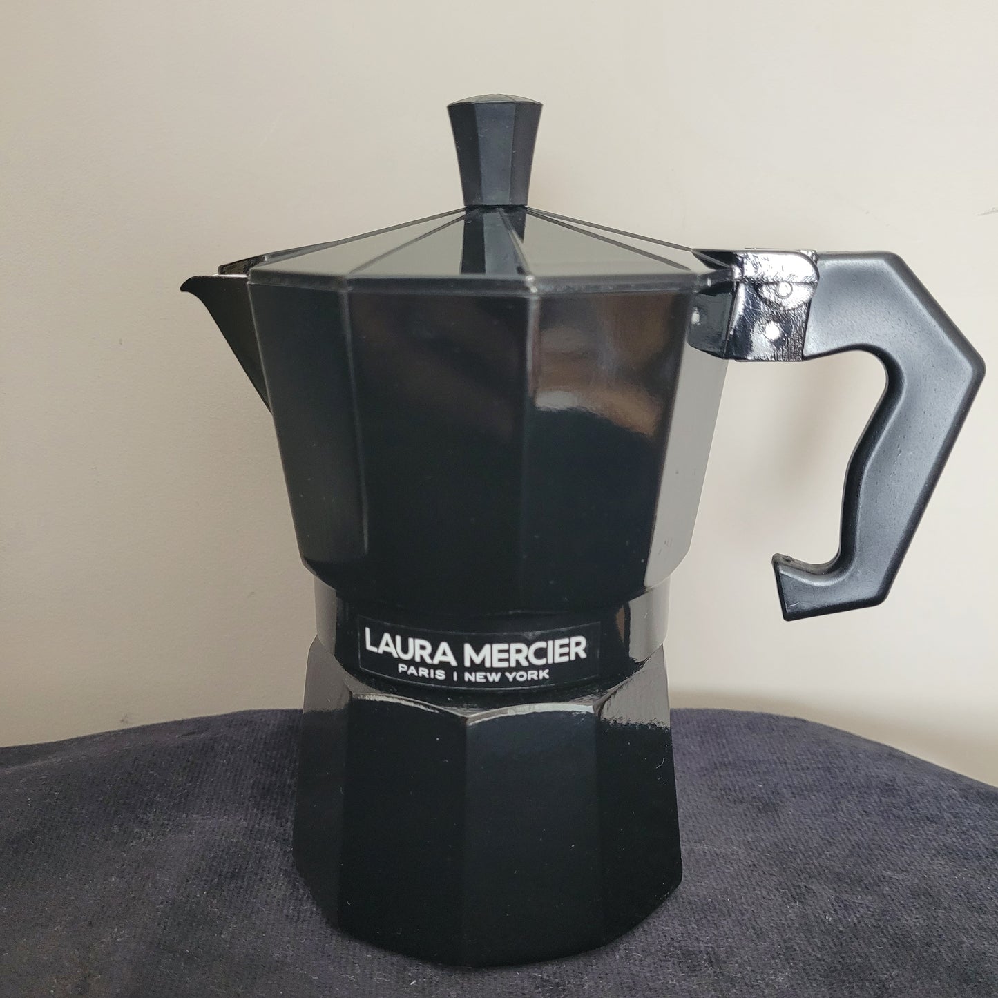 Eleganter Espressokocher Laura Mercier Design in Schwarz mit sechseckiger Form und hochwertigem Finish. Die stilvolle Kanne trägt die Markensignatur Laura Mercier Paris | New York und steht auf einer dunklen Oberfläche mit hellem Hintergrund. Perfekte Kombination aus modernem Design und Kaffeegenuss für echte Liebhaber.