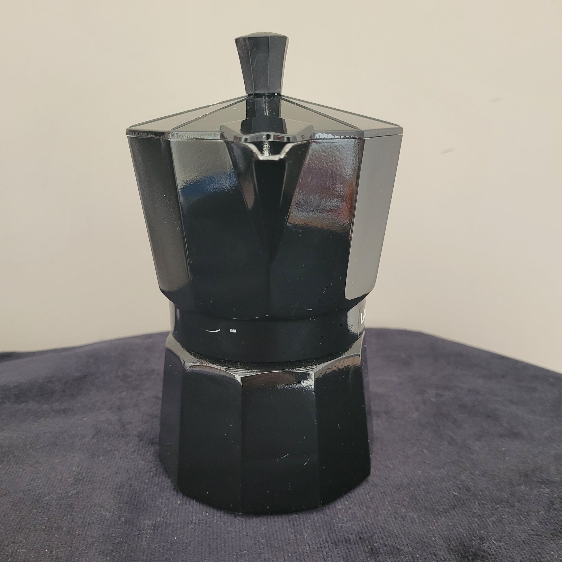 Vorderansicht des eleganten Espressokochers Laura Mercier Design in Schwarz, mit sechseckigem Gehäuse und hochwertigem Finish. Der Schriftzug Laura Mercier Paris | New York ist auf der Vorderseite deutlich sichtbar. Der schwarze Griff und Deckel ergänzen das stilvolle Design. Perfekt für Liebhaber von edlem Kaffeezubehör und stilvollem Genuss.