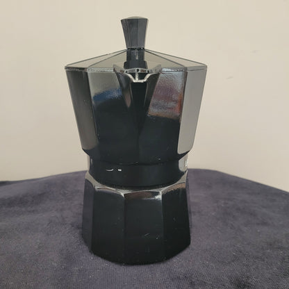 Vorderansicht des eleganten Espressokochers Laura Mercier Design in Schwarz, mit sechseckigem Gehäuse und hochwertigem Finish. Der Schriftzug Laura Mercier Paris | New York ist auf der Vorderseite deutlich sichtbar. Der schwarze Griff und Deckel ergänzen das stilvolle Design. Perfekt für Liebhaber von edlem Kaffeezubehör und stilvollem Genuss.