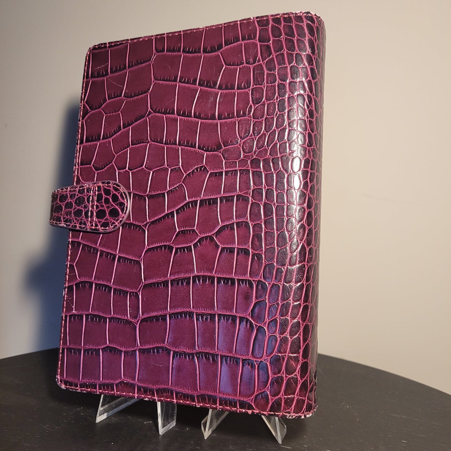 Eleganter Filofax Osterley Personal Organiser aus lila italienischem Kalbsleder mit glänzender Krokodilleder-Optik und Verschlusslasche, auf dunklem Hintergrund.