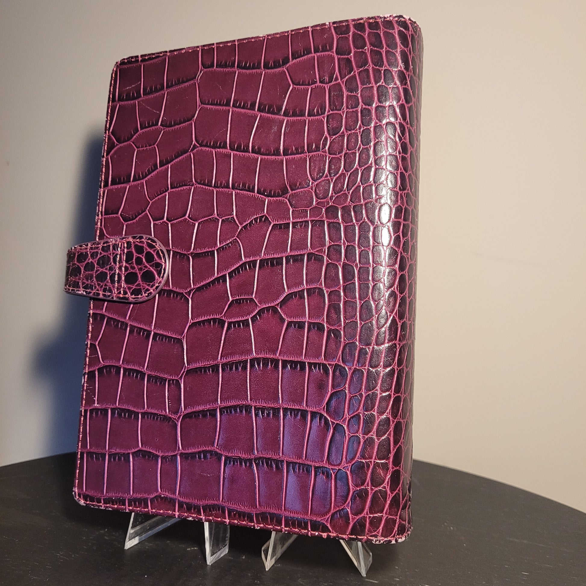 Eleganter Filofax Osterley Personal Organiser aus lila italienischem Kalbsleder mit glänzender Krokodilleder-Optik und Verschlusslasche, auf dunklem Hintergrund.