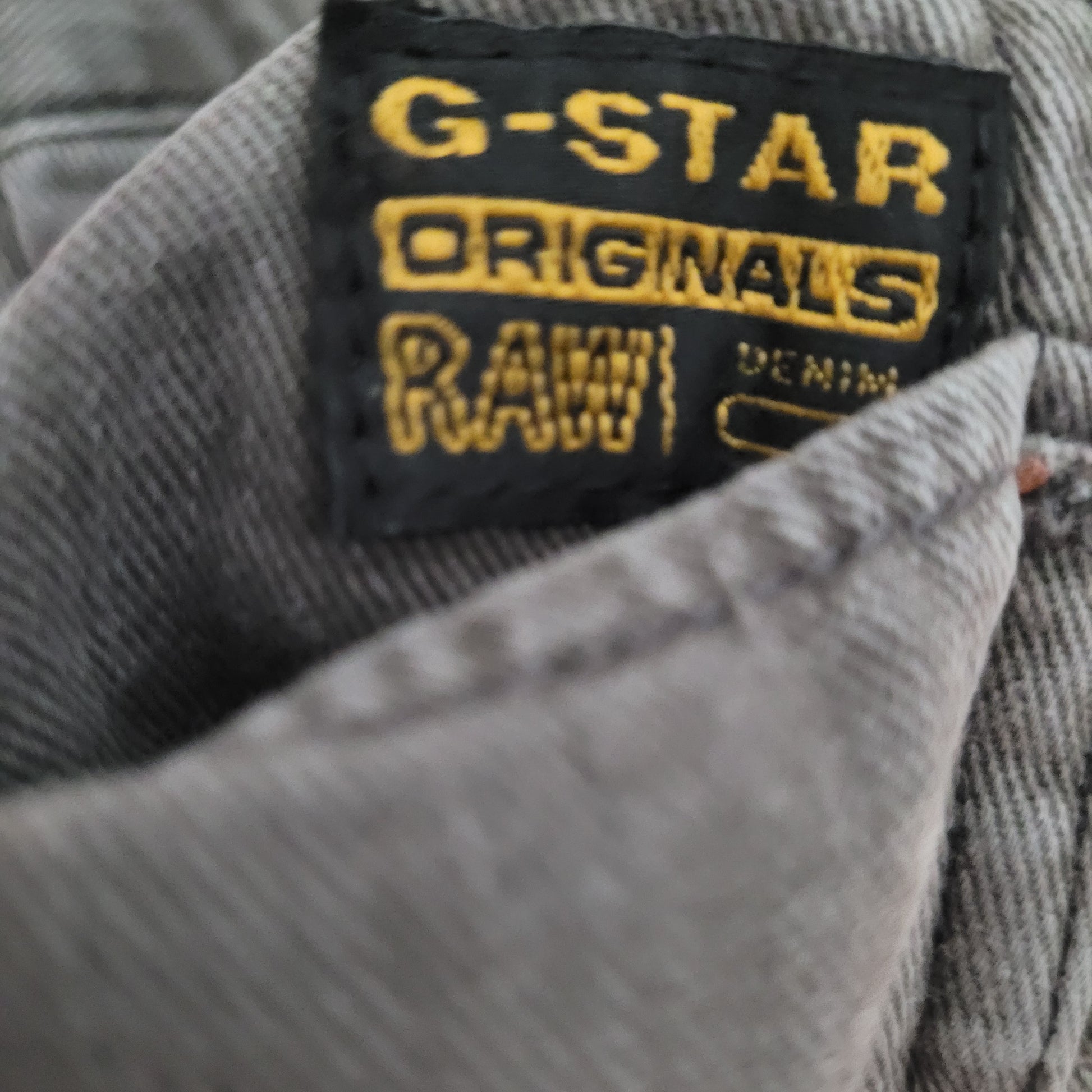 Markenbezeichnung "GStar Raw Originals Denim" auf schwarzem Hintergrund und goldener Schrift zu sehen