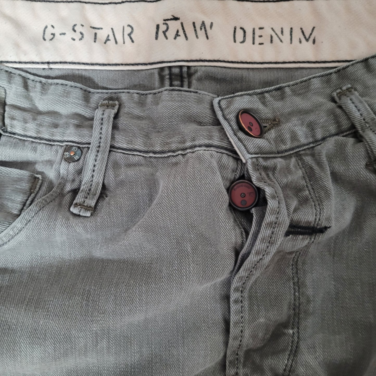 Zu sehen ist die vordere Oberseite. 2 Knöpfe sowie die Bezeichnung G-Star Raw Denim in der Innenseite zu lesen.