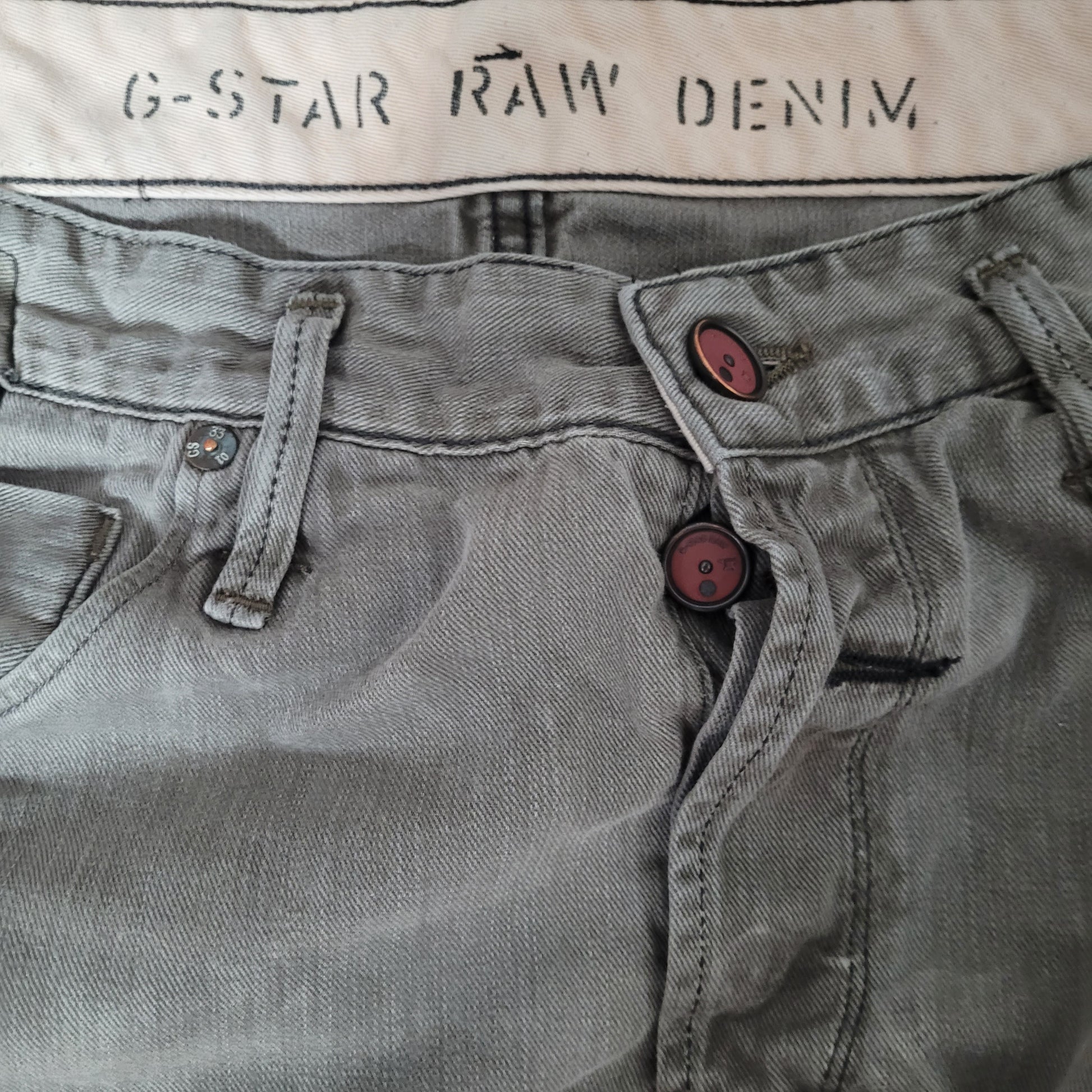 Zu sehen ist die vordere Oberseite. 2 Knöpfe sowie die Bezeichnung G-Star Raw Denim in der Innenseite zu lesen.