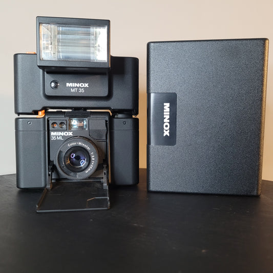 Minox 35 ML Kamera mit Minox MT 35 Blitzgerät und Schutzhülle auf schwarzem Untergrund.
