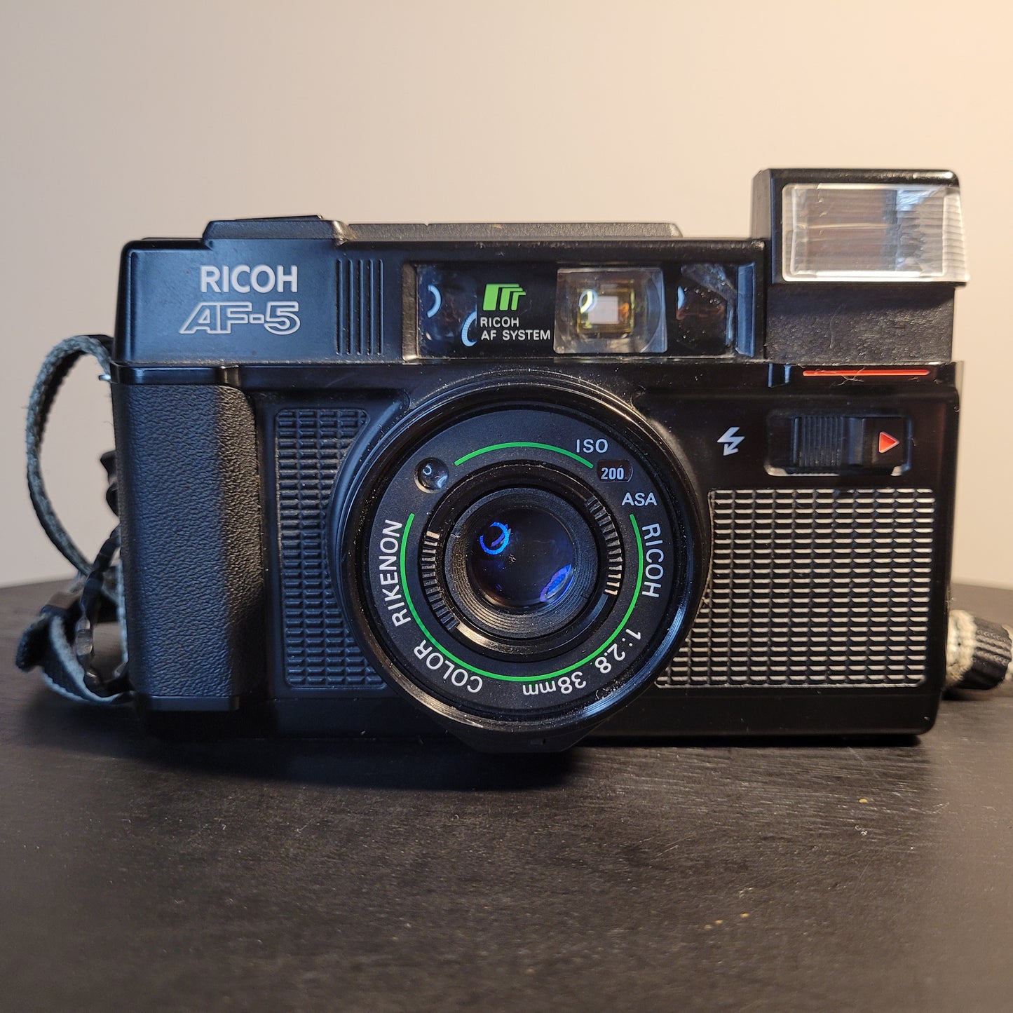 Nahaufnahme einer Ricoh AF-5 Kamera mit Rikenon 1:2.8 38mm Objektiv, ISO 200 Einstellung und integriertem Blitz.
