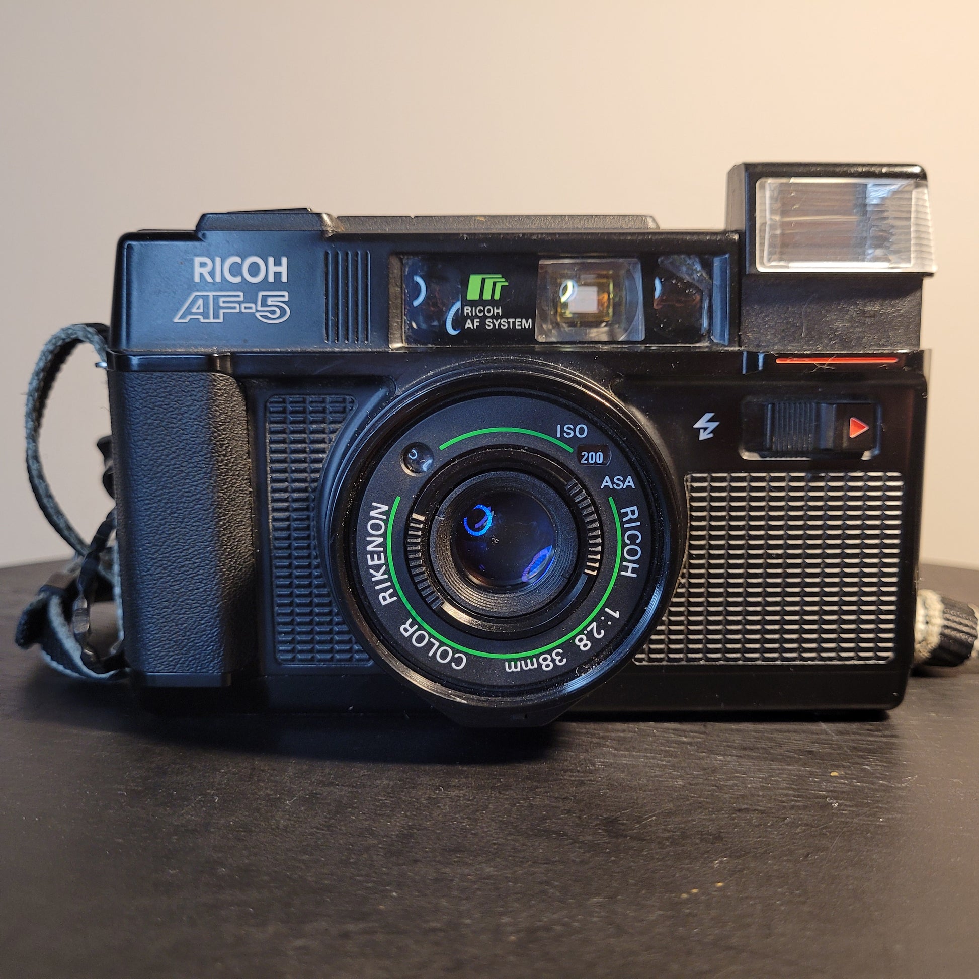 Nahaufnahme einer Ricoh AF-5 Kamera mit Rikenon 1:2.8 38mm Objektiv, ISO 200 Einstellung und integriertem Blitz.