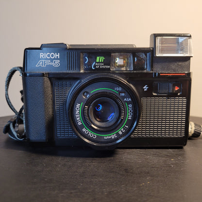 Nahaufnahme einer Ricoh AF-5 Kamera mit Rikenon 1:2.8 38mm Objektiv, ISO 200 Einstellung und integriertem Blitz.