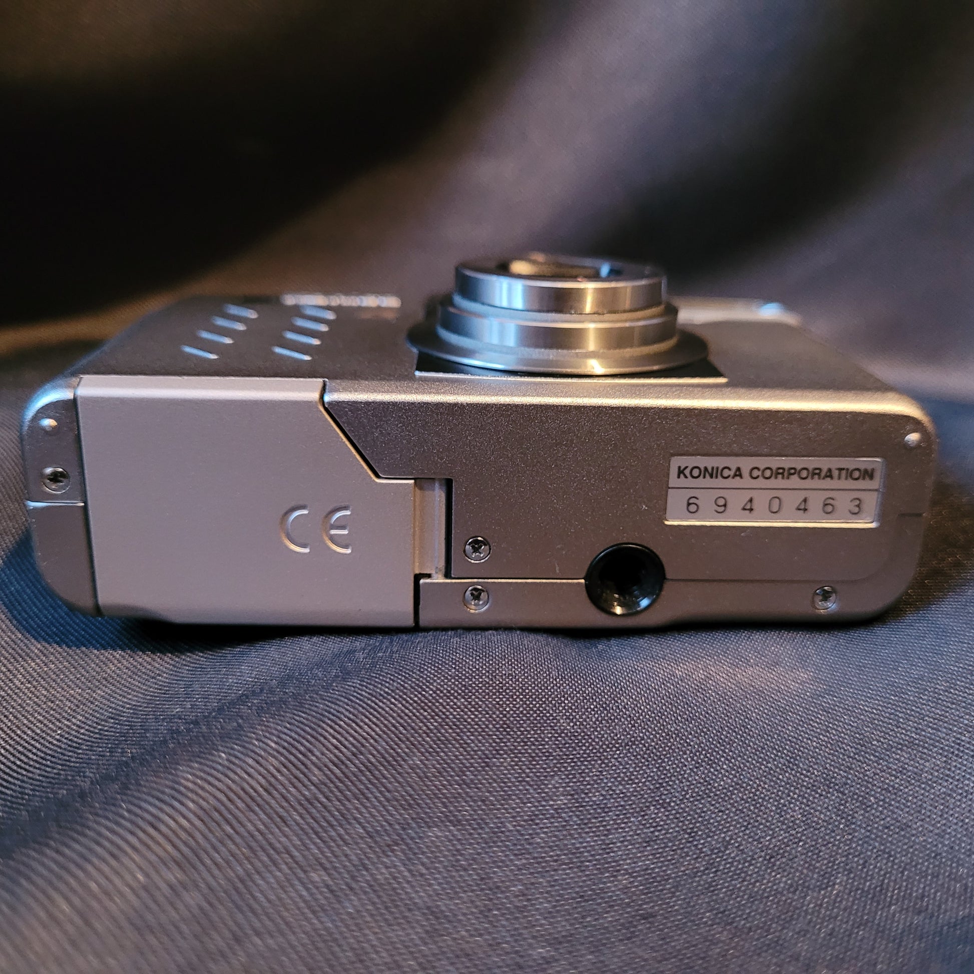 Untere Seite der Konica Revio Kamera mit Batteriefach, CE-Kennzeichnung, Stativgewinde und Seriennummer 6940463. Vintage Kamera mit silbernem Gehäuse.