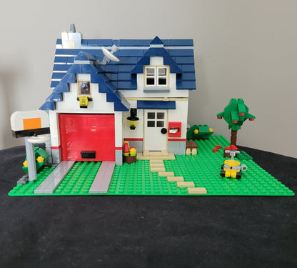 Das LEGO Creator Modell 5891 - Haus mit Garage – detailreiches Einfamilienhaus mit blauen Dachziegeln, rotem Garagentor und liebevoll gestalteter Umgebung inklusive Baum, Briefkasten und Rasenmäher. Perfektes Set für LEGO-Fans und Sammler! EAN: 5702014600546.
