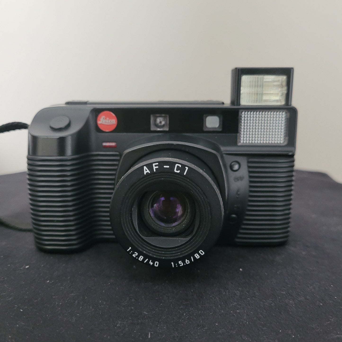 Leica Vintage Analogkamera AF-C1 in Schwarz mit integriertem Blitz und Dual-Objektiv (40 mm f/2.8 & 80 mm f/5.6), präsentiert auf dunkler Oberfläche – klassische Leica Kompaktkamera für analoge Fotografie mit ikonischem Retro-Design und rotem Leica-Logo.