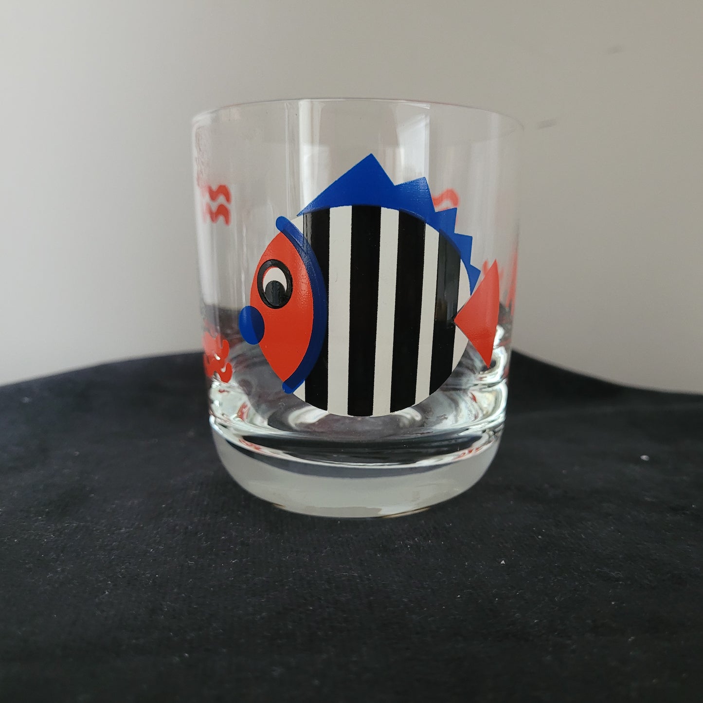 Vintage Trinkglas mit Fischmotiv – Stilvolles Design auf schwarzer Oberfläche Das Bild zeigt ein Vintage Trinkglas mit Fischmotiv, platziert auf einer schwarzen Oberfläche mit grauem Hintergrund. Das Glas besticht durch sein klassisches Design und die detailreiche Abbildung eines Fisches, die dem Set eine besondere Note verleiht.