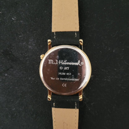 Das Bild zeigt die Rückseite einer M.J. Hummel Vintage Armbanduhr mit einem goldfarbenen Gehäuse und einem schwarzen Lederarmband. Dezent eingravierte Informationen, darunter „M.J. Hummel“, „© 2015“, „HUM 451“, „Nur ein Venedigsmädchen“ und „CE“, sind auf der Rückseite deutlich zu erkennen.