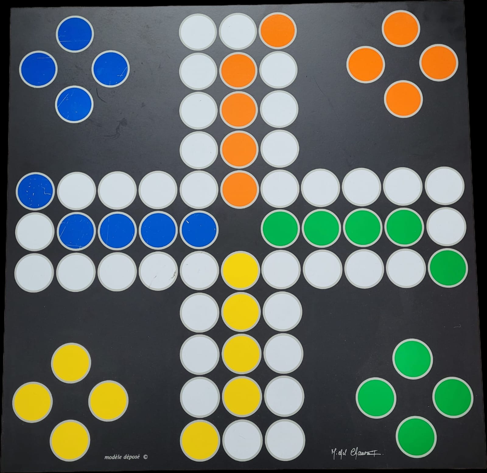 Das Bild zeigt die Vorderseite des Gesellschaftsspiels "Decoplay", gestaltet von Michel Chauvaux, mit Zwergfiguren von Deco Play. Das Spielbrett ist auf einem schwarzen Untergrund platziert. Die Signatur von Michel Chauvaux ist sichtbar und verleiht dem Design eine besondere Authentizität.