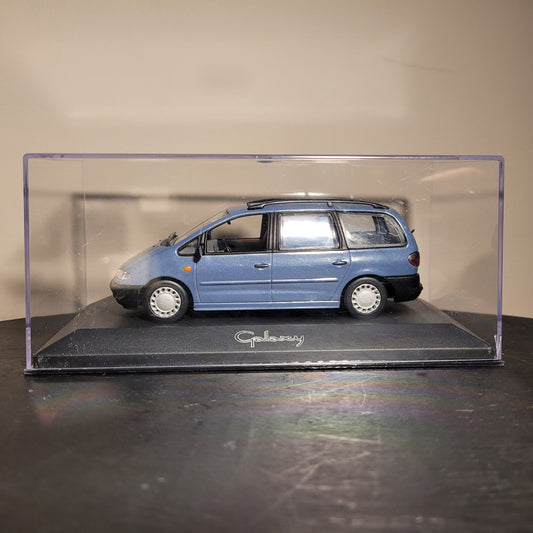 Ein Modellauto eines blauen Ford Galaxy in einer durchsichtigen Vitrine. Das Modell zeigt detaillierte Merkmale wie Fenster, Räder und Scheinwerfer. Die Vitrine steht auf einem schwarzen Sockel mit der Aufschrift "Galaxy".