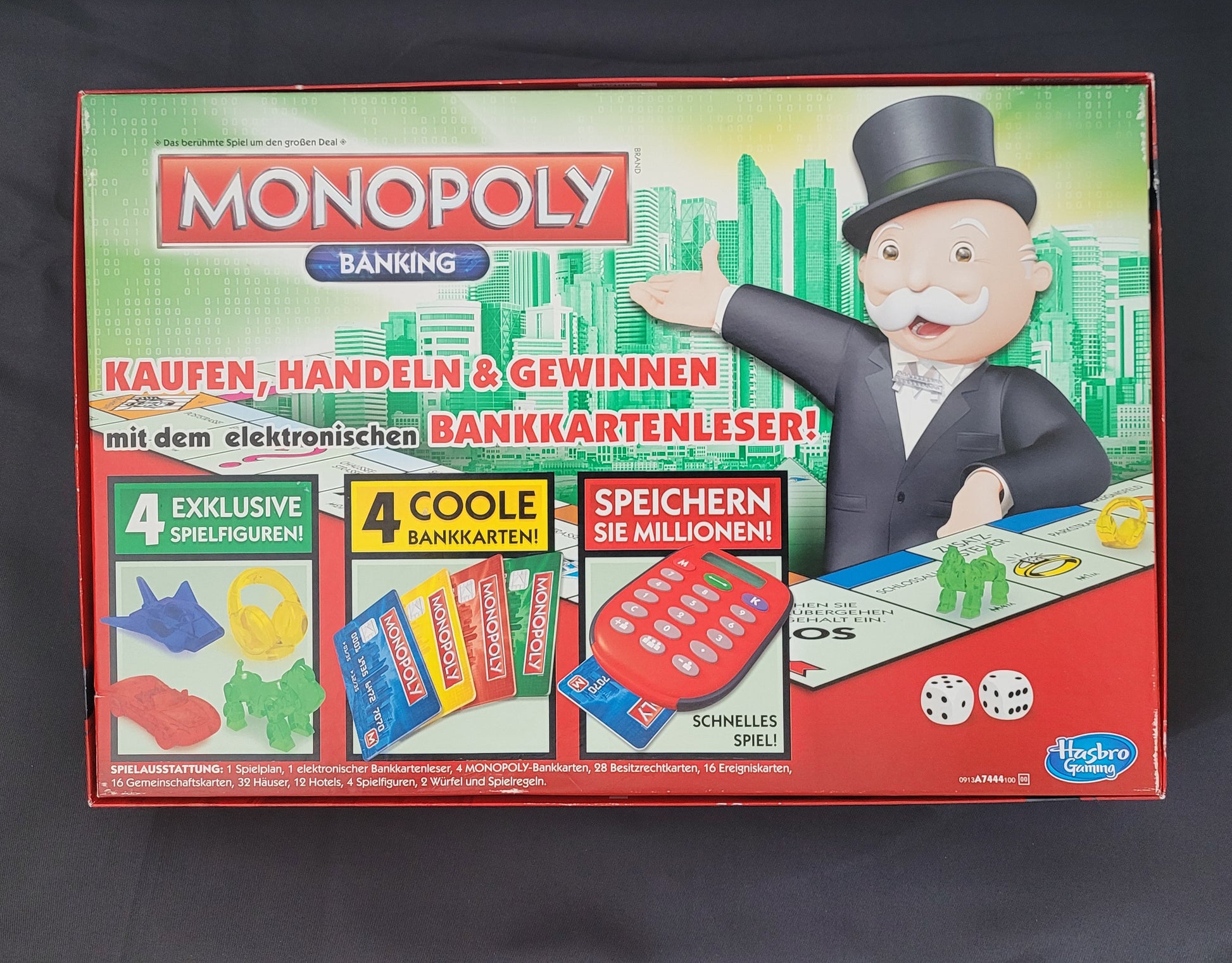 Das Bild zeigt die Rückseite des Monopoly Banking Gesellschaftsspiels von Hasbro. Sichtbar sind die detaillierten Informationen zum Spielablauf sowie die einzelnen Spielfunktionen, die auf der Verpackung beschrieben sind. Das Design der Verpackungsrückseite bietet eine klare Übersicht über die enthaltenen Komponenten und Features des Monopoly Banking Spiels. Das Bild ist auf einem dunklen Untergrund platziert, wodurch die Farben und Details besonders gut zur Geltung kommen.