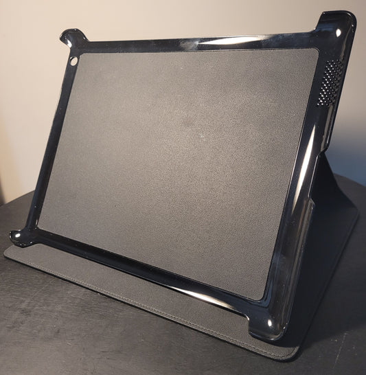 Montblanc Tablet Halter für iPad 3 aus schwarzem Leder mit strukturierter Rückseite, glänzender Kunststoffumrandung und Lüftungsschlitzen, auf einem Tisch stehend.
