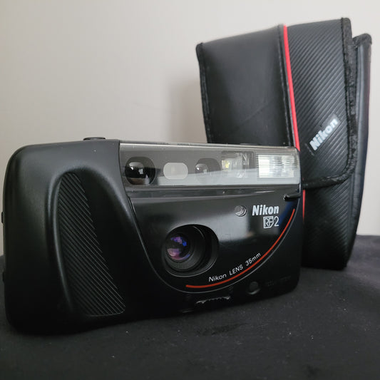Eine hochwertige Nikon RF2 Kamera mit einem 35mm Objektiv und einem eleganten schwarzen Gehäuse mit roten Akzenten, präsentiert neben einer stilvollen schwarzen Nikon Kameratasche mit rotem Streifen und Nikon-Logo.