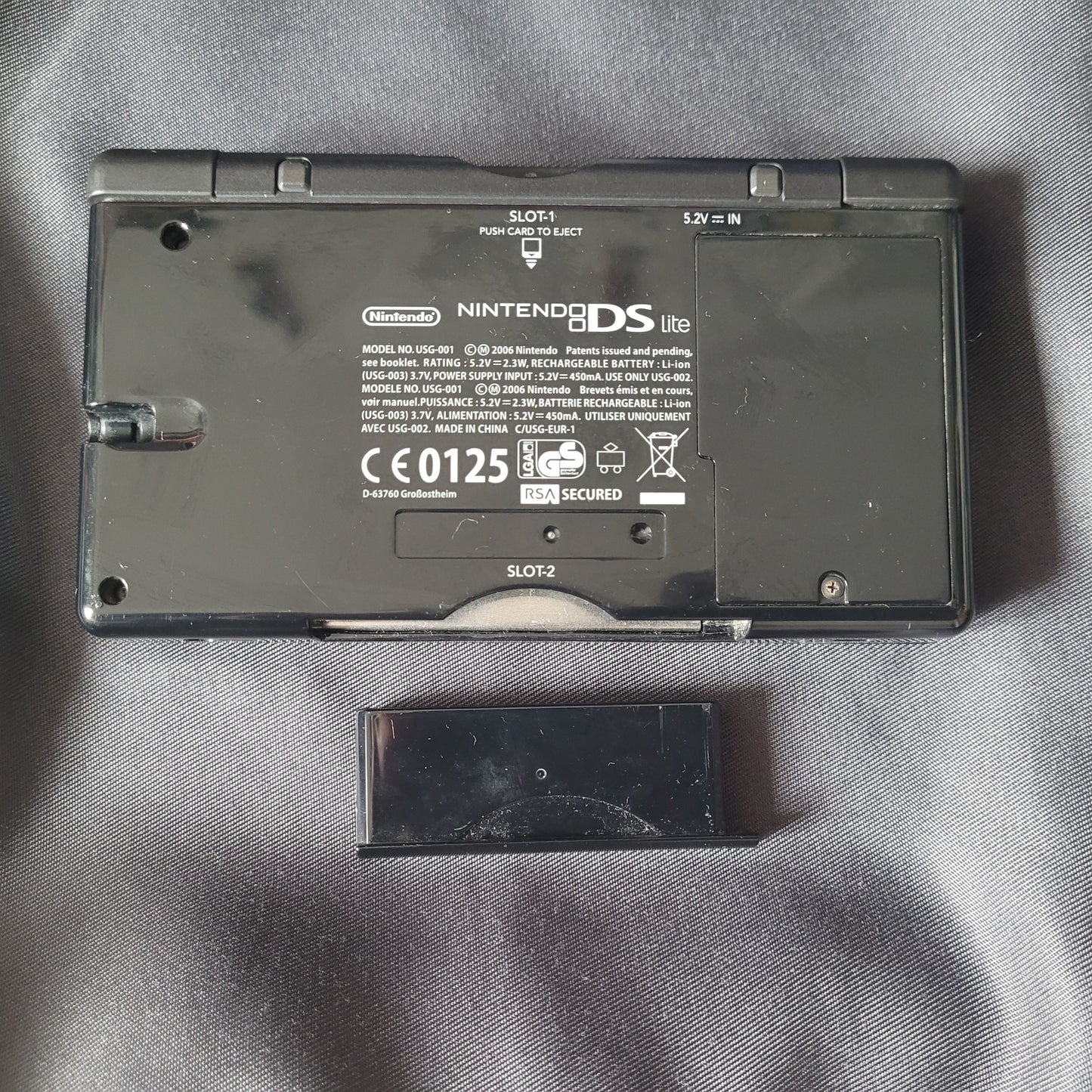 Nintendo DS Lite Konsole Schwarz – Modell USG‑001 – Vintage Handheld, Unterseite mit geöffnetem SLOT‑2‑Schacht für Game‑Boy‑Advance‑Module, technische Angaben und CE‑Kennzeichnung sichtbar.