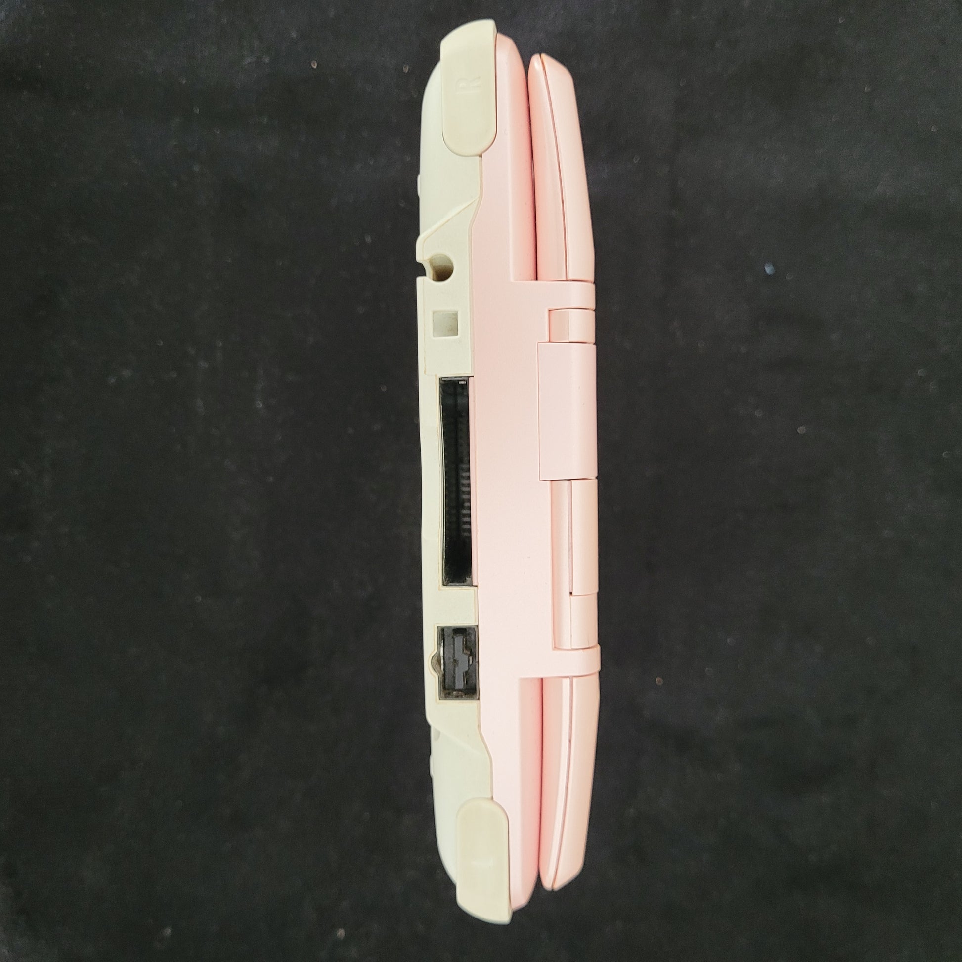 Seitenansicht der Nintendo DS Pink Model No NTR-001 Handheld Konsole, liegend auf schwarzem Untergrund. 