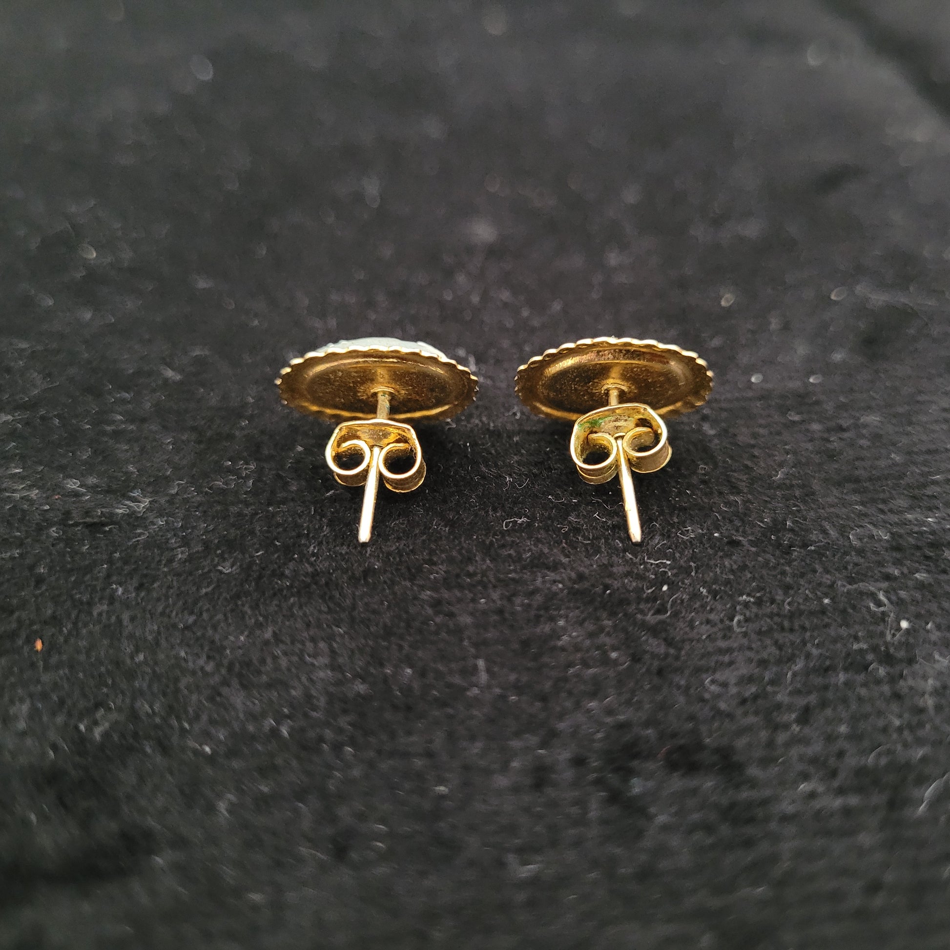 Rückseite von zwei goldenen Ohrringen auf schwarzem Hintergrund. Die Ohrringe haben eine runde Form mit gezacktem Rand und dekorativen Verschlüssen.