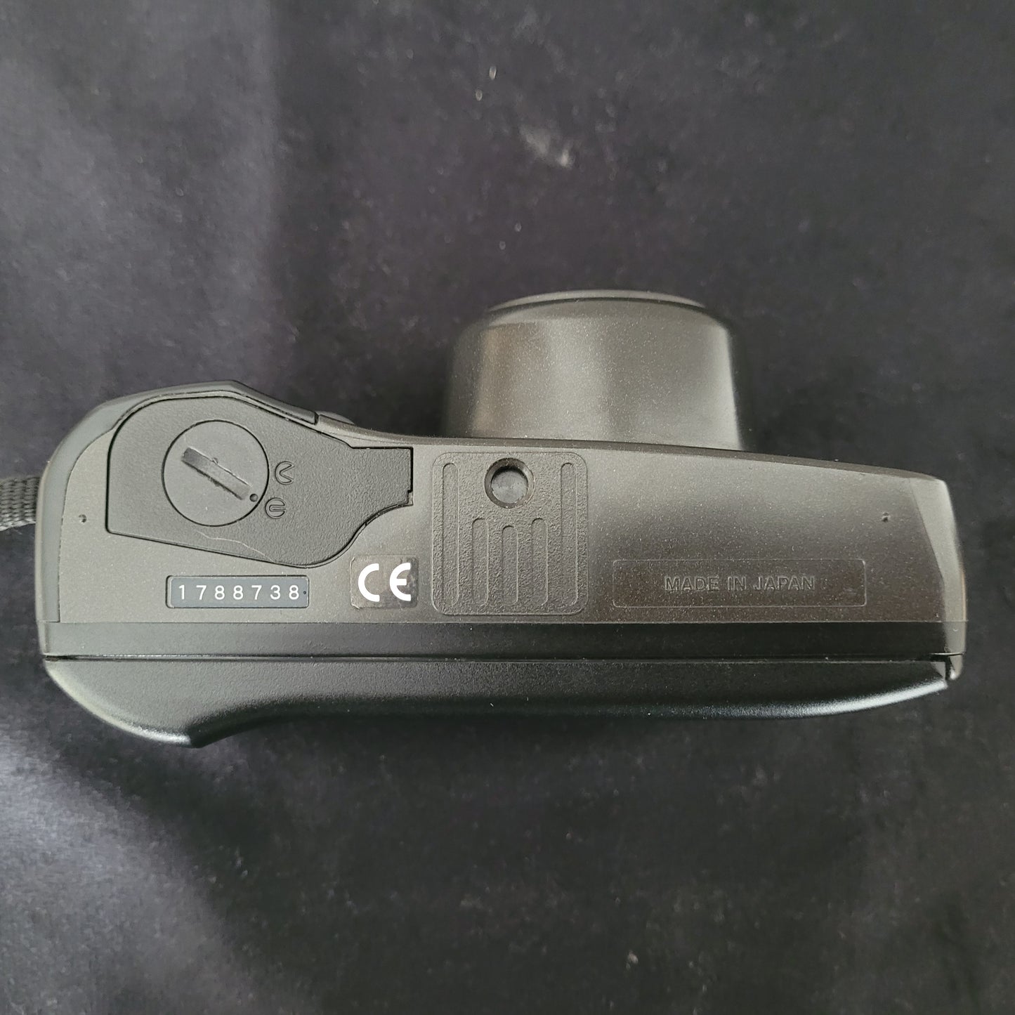 Unterseite der Olympus Superzoom 120 Multi AF Analogkamera mit sichtbarem Batteriefach und der Aufschrift Made in Japan. Die Vintage Analogkamera zeigt ihr robustes Design und präzise Verarbeitung. Perfekt für Liebhaber klassischer Analogfotografie mit authentischer Qualität.