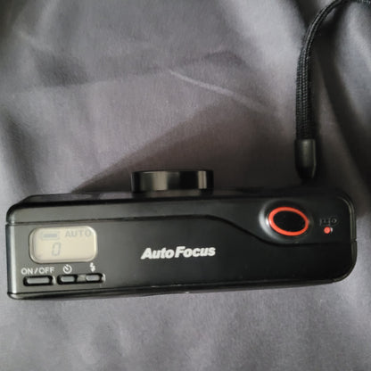 Panasonic Super Mini C-625AF Vintage Analogkamera Draufansicht mit Display, ON/OFF-Taste, rotem Auslöser und Handgelenkschlaufe – kompakte 35mm Autofokus-Kamera für Sammler klassischer Fototechnik.