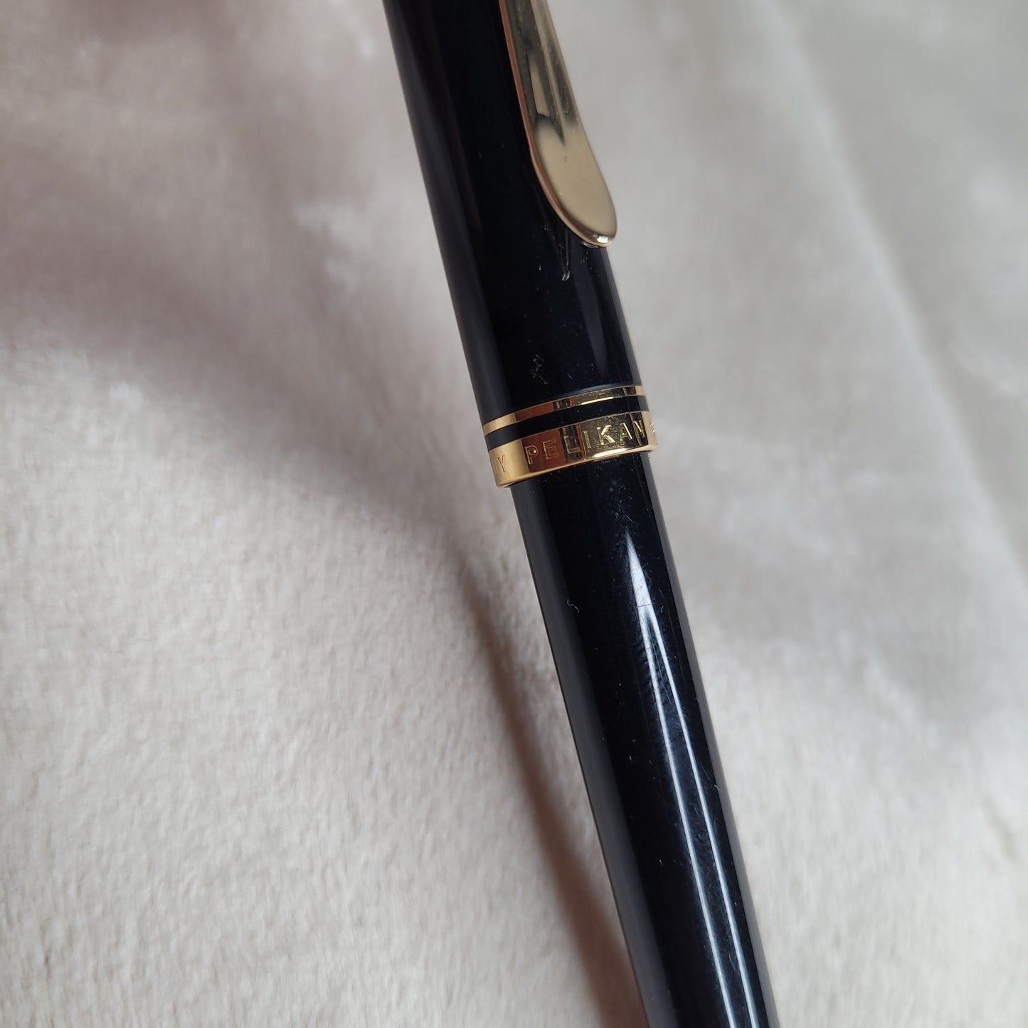 Nahaufnahme eines Pelikan Druckbleistifts Souverän D405 in schwarz mit goldenen Akzenten, inklusive gravierter 'Pelikan'-Aufschrift auf dem goldenen Band, auf einer hellen, weichen Textur platziert. Elegantes und hochwertiges Design.