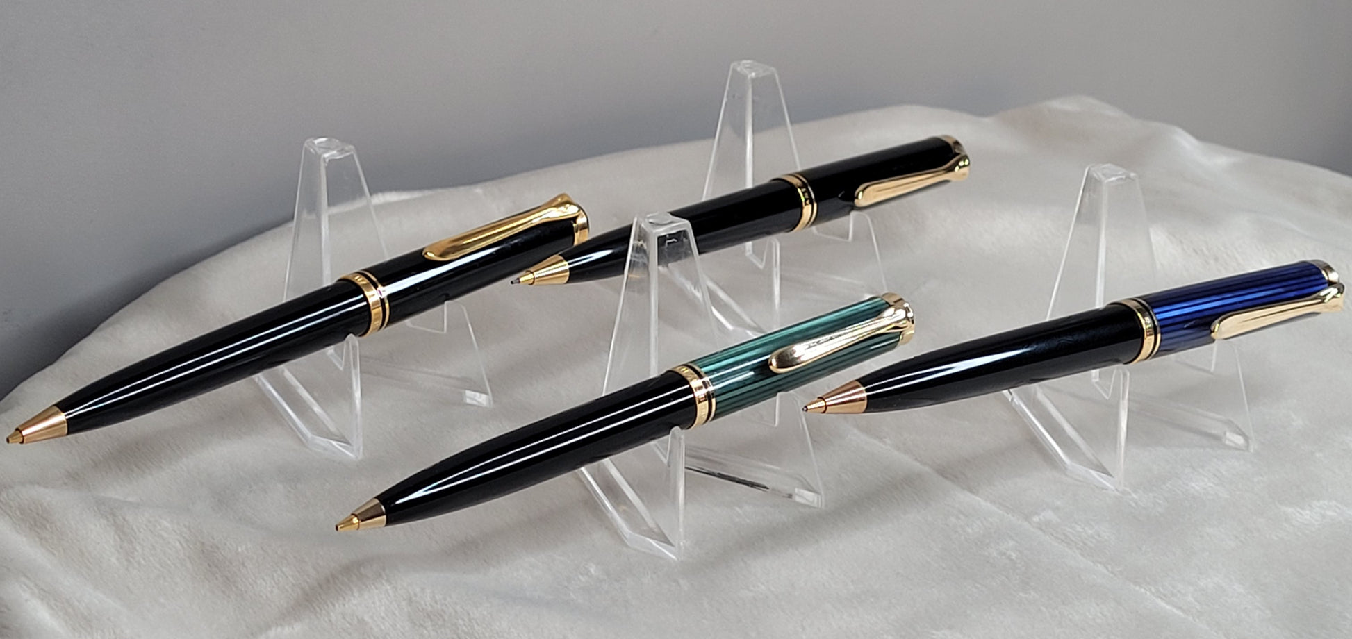 Vier hochwertige Pelikan Souverän Drehbleistifte in verschiedenen Modellen, präsentiert auf durchsichtigen Kunststoffständern. Die Stifte bestechen durch ihr elegantes Design in Schwarz, Blau und Grün, verziert mit goldenen Akzenten und verzierten Clips. Diese luxuriösen Schreibgeräte, hergestellt in Deutschland, stehen für höchste Verarbeitungsqualität und Präzision. Ideal als stilvolles Accessoire für das Büro oder als luxuriöses Geschenk.