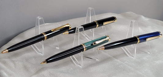 Vier hochwertige Pelikan Souverän Drehbleistifte in verschiedenen Modellen, präsentiert auf durchsichtigen Kunststoffständern. Die Stifte bestechen durch ihr elegantes Design in Schwarz, Blau und Grün, verziert mit goldenen Akzenten und verzierten Clips. Diese luxuriösen Schreibgeräte, hergestellt in Deutschland, stehen für höchste Verarbeitungsqualität und Präzision. Ideal als stilvolles Accessoire für das Büro oder als luxuriöses Geschenk.