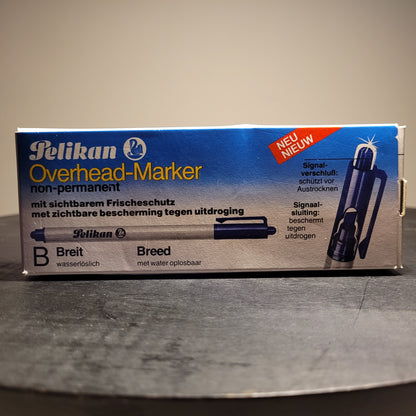 Die Abbildung zeigt eine Verpackung eines Pelikan Overhead-Markers. Der Marker ist nicht permanent und wasserlöslich. Auf der Verpackung steht „Pelikan Overhead-Marker non-permanent“ und „mit sichtbarem Frischeschutz“ sowie „mit zichtbare bescherming tegen uitdroging“. Es gibt auch einen Hinweis „NEU“ in der oberen rechten Ecke. Der Marker hat eine breite Spitze („B Breit“ und „Breed“) und ist wasserlöslich („wasserlöslich“ und „met water oplosbaar“).