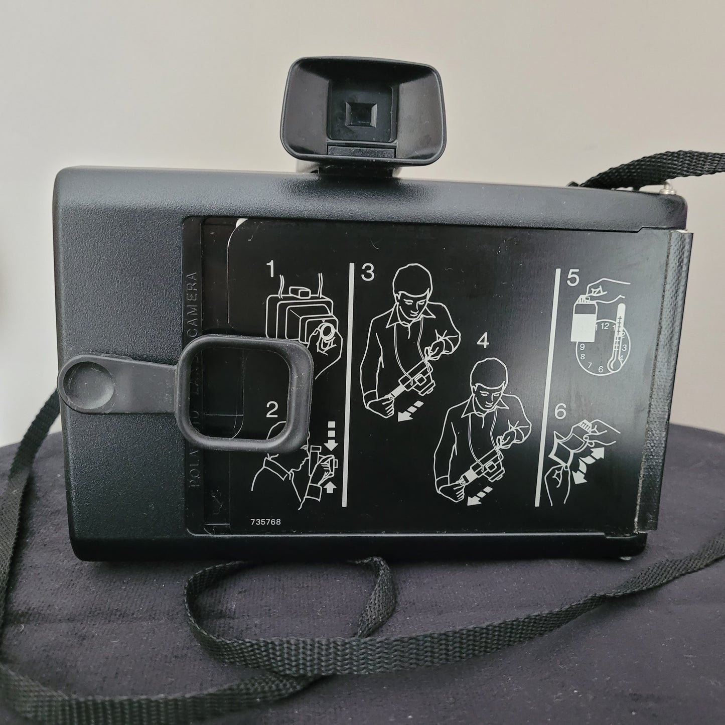Rückseite der Polaroid Sofortbildkamera Instant 30. Abbildung zeigt die Bedienungsanleitung mit sechs Schritten zur Handhabung, inklusive Filmeinlegen und Belichtungsmessung. Kamera mit Sucher und Trageriemen.