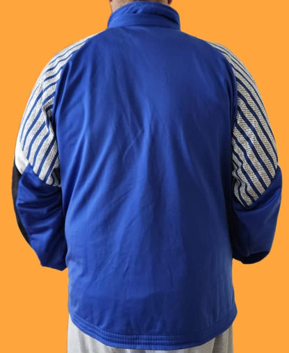 Rückansicht einer blauen Fleecejacke mit weiß-schwarz gestreiften Ärmeln und hohem Kragen, kombiniert mit hellgrauer Hose – sportlicher Look vor orangefarbenem Hintergrund.