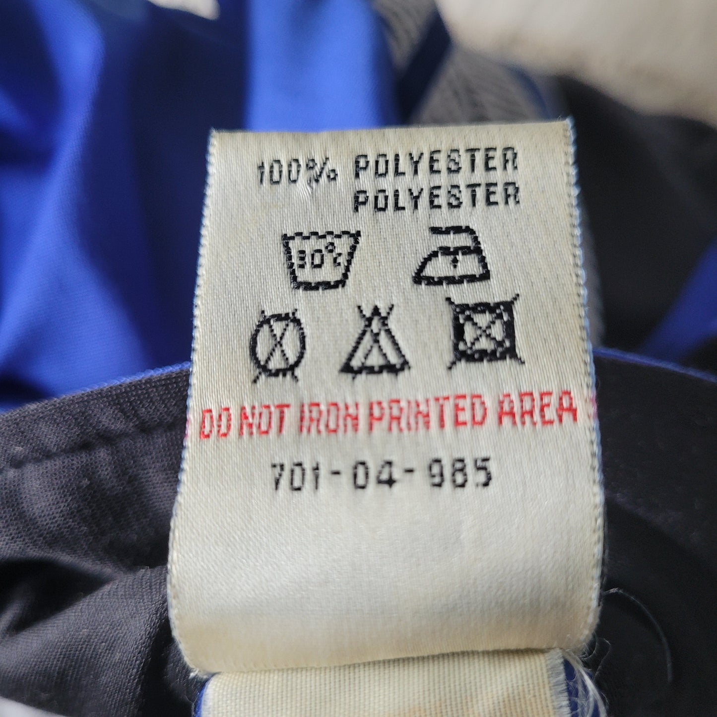 Pflegeetikett aus 100 % Polyester mit Waschhinweisen: 30 °C Maschinenwäsche, kein Bleichen, kein Trockner, nicht bügeln, keine chemische Reinigung – roter Hinweis „DO NOT IRON PRINTED AREA“, Code: 701-04-985