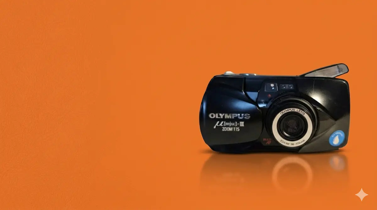 Schwarze Olympus mju II Zoom 115 Analogkamera auf orangefarbenem Hintergrund – Geprüfte Vintage-Kameras und Sammlerstücke von RAVIFY.