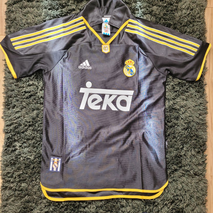 intage Real Madrid Trikot Raul Saison 1999/2000 in Größe S, ausgelegt auf grünem Teppich. Das dunkelgraue Adidas-Trikot mit gelben Streifen und Teka-Sponsorlogo zeigt das klassische Design der frühen 2000er und ist ein begehrtes Sammlerstück für Fans und Liebhaber von Real Madrid Vintage Fußballtrikots.