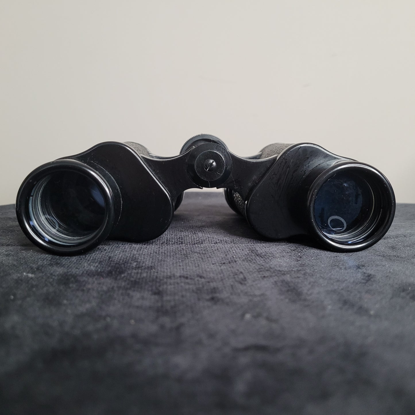 Ein schwarzes Revue 8x30 Fernglas liegt auf einer dunklen Oberfläche. Die Okulare und Objektive des Fernglases sind deutlich sichtbar. Das Fernglas hat eine kompakte, klassische Form und ist aus Metall und Kunststoff gefertigt, ideal für Outdoor-Aktivitäten wie Vogelbeobachtung oder Wandern.