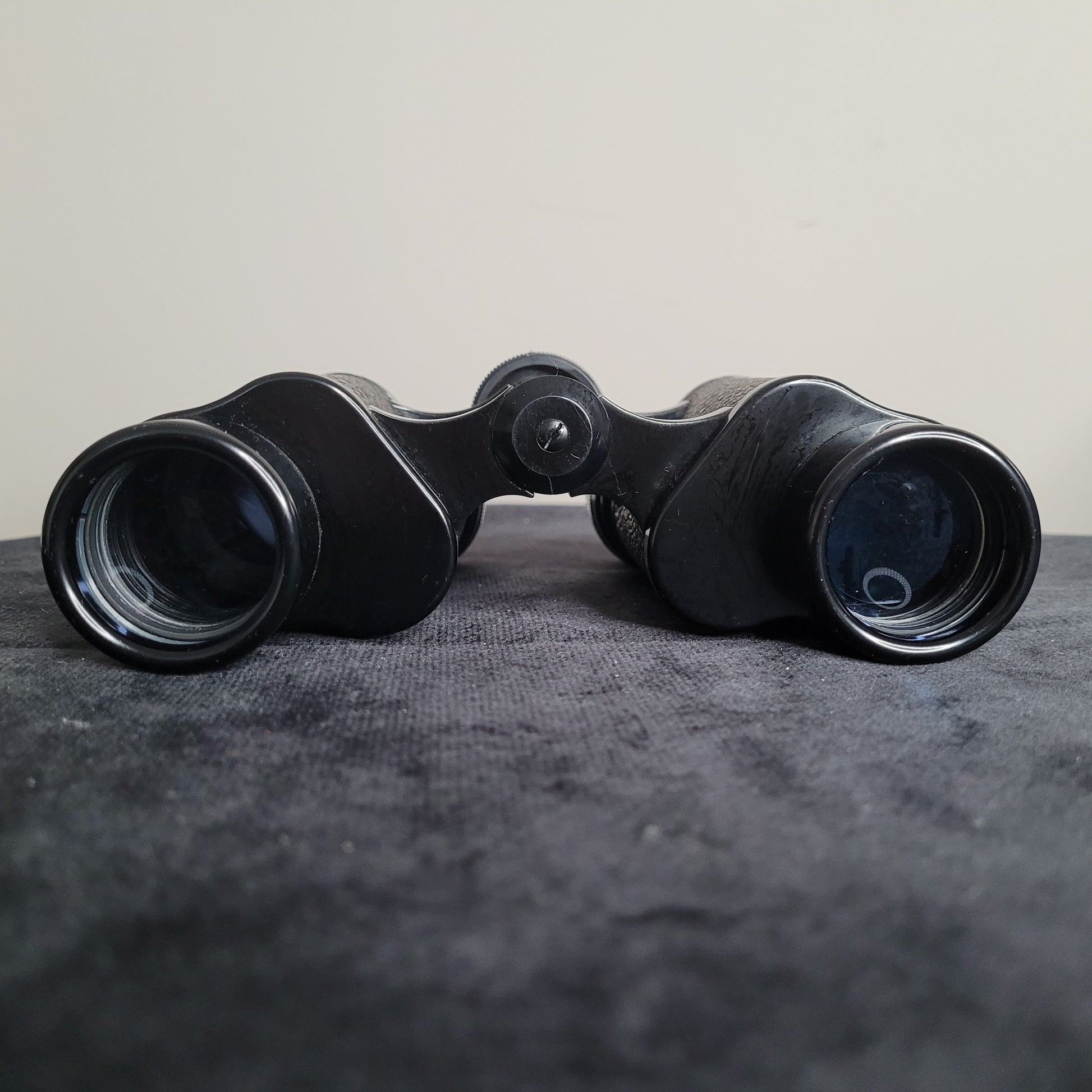 Ein schwarzes Revue 8x30 Fernglas liegt auf einer dunklen Oberfläche. Die Okulare und Objektive des Fernglases sind deutlich sichtbar. Das Fernglas hat eine kompakte, klassische Form und ist aus Metall und Kunststoff gefertigt, ideal für Outdoor-Aktivitäten wie Vogelbeobachtung oder Wandern.
