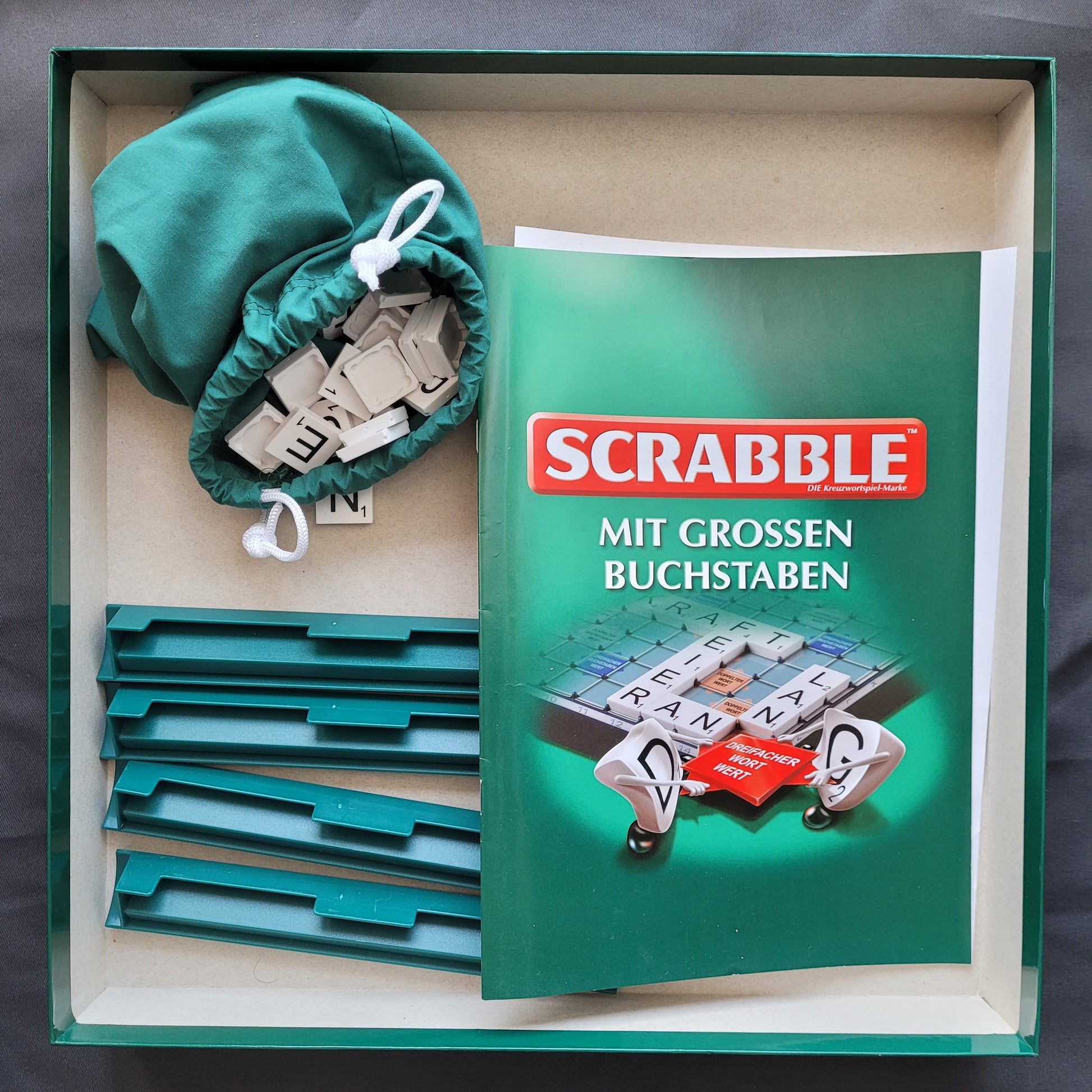 Das Bild zeigt die Innenansicht des Scrabble mit großen Buchstaben – ein hochwertiges Gesellschaftsspiel von Piatnik & Mattel. Sichtbar sind das geöffnete Spielbrett sowie die extra großen Buchstabensteine, die für bessere Lesbarkeit sorgen. Die stabile Spielfläche und die gut sortierte Innenaufteilung erleichtern das Spiel und die Handhabung. Der Hintegrund ist schwarz.