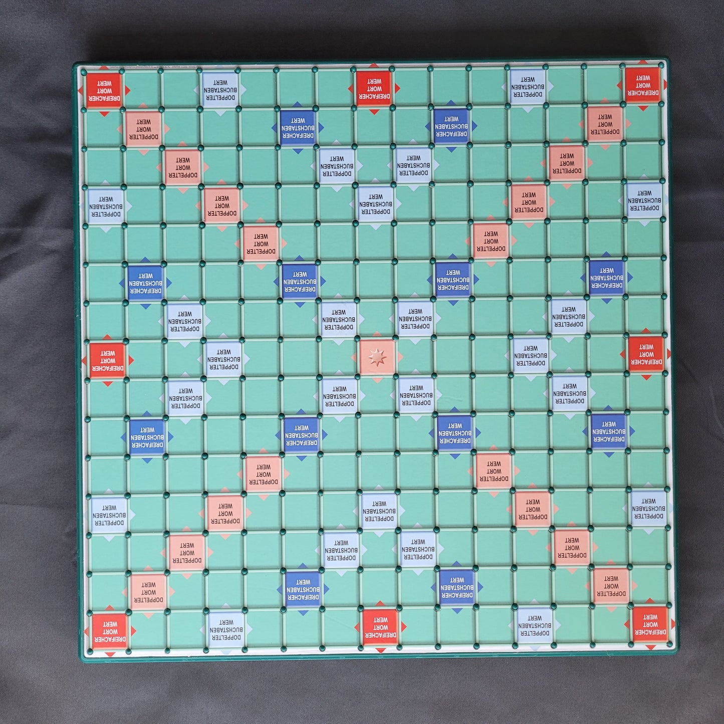 Das Bild zeigt das Spielbrett des Scrabble mit großen Buchstaben – ein hochwertiges Gesellschaftsspiel von Piatnik & Mattel. Die Spielfläche ist mit dem klassischen Scrabble-Design bedruckt und bietet ausreichend Platz für die extra großen Buchstabensteine, die für eine besonders gute Lesbarkeit sorgen. Die stabile und rutschfeste Oberfläche erleichtert das Platzieren der Spielsteine und sorgt für ein angenehmes Spielerlebnis. Der Hintergrund ist schwarz.
