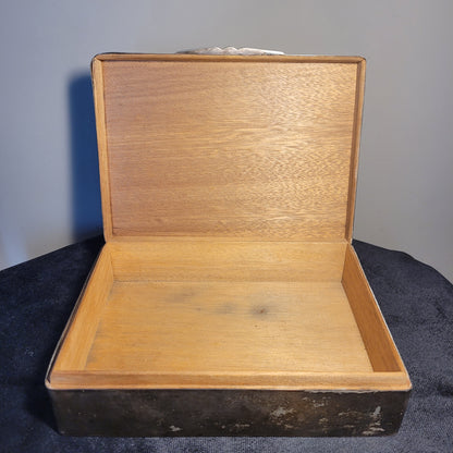 Innenseite einer rechteckigen Holzkiste mit glatter, heller Oberfläche und dunklen Flecken auf der rechten Seite, auf dunklem Stoffhintergrund