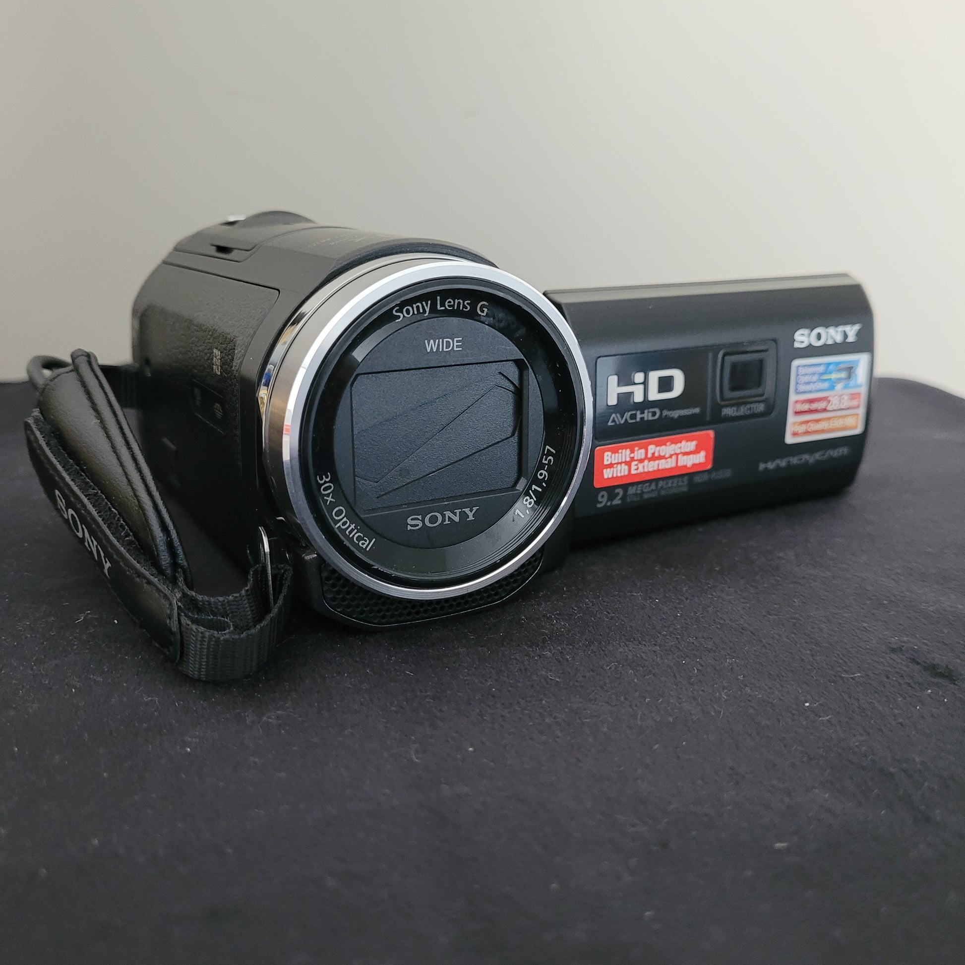 Die Sony Handycam HDR-PJ530E liegt auf einer schwarzen Oberfläche und zeigt ihre Funktionen wie 30-fachen optischen Zoom, integrierten Projektor, 9,2-Megapixel-Exmor-R-CMOS-Sensor sowie AVCHD Progressive Technologie. Perfekt für gestochen scharfe HD-Aufnahmen und Projektionen, ideal für Film- und Fotobegeisterte.