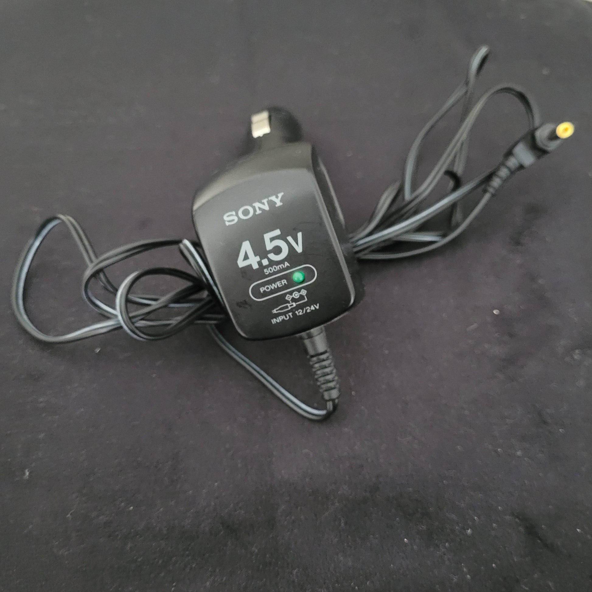 Sony Netzteil mit 4,5V Ausgangsspannung für Vintage Discman CD-Player, schwarzes Gehäuse mit deutlich sichtbarem Sony-Logo und gelber Anschlussbuchse. Auf der Vorderseite befinden sich LED-Anzeigen für „POWER“ (grün) und „CHARGE“ (rot) sowie die Beschriftung „4.5V“ und „INPUT: 12V“. Das originale Sony Netzteil ist passend für Modelle wie den Sony Vintage Discman Mega Bass Model D-121 und unterstreicht die authentische Ausstattung klassischer tragbarer Audiogeräte der 1990er Jahre.