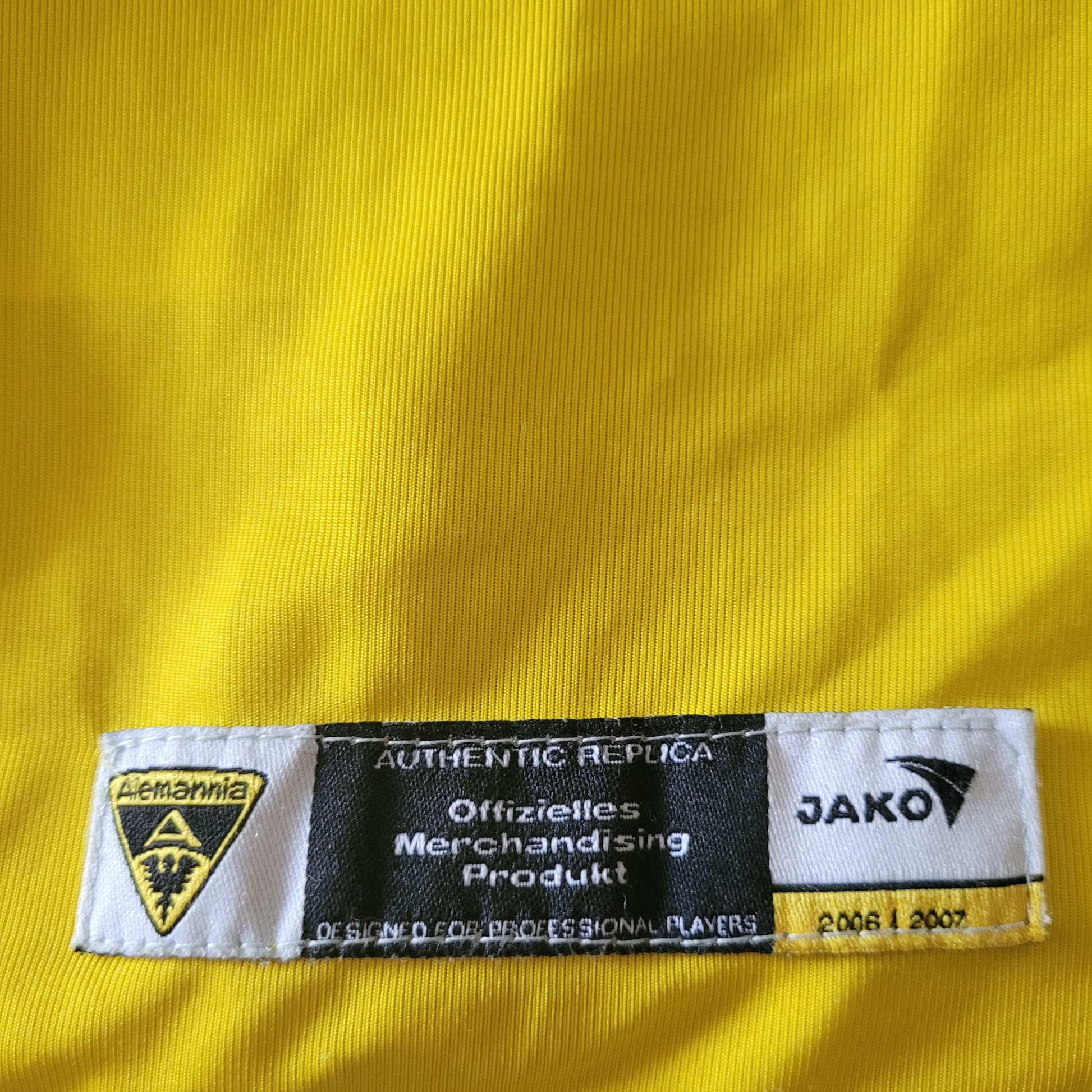 Etikett mit folgendem Hinweis istzu sehen: Authentic Replica; Offizielles Merchandising Produkt. Zusätzlich ist das Logo des TSV Alemannia Aachen und des Herstellers Jako zu sehen.