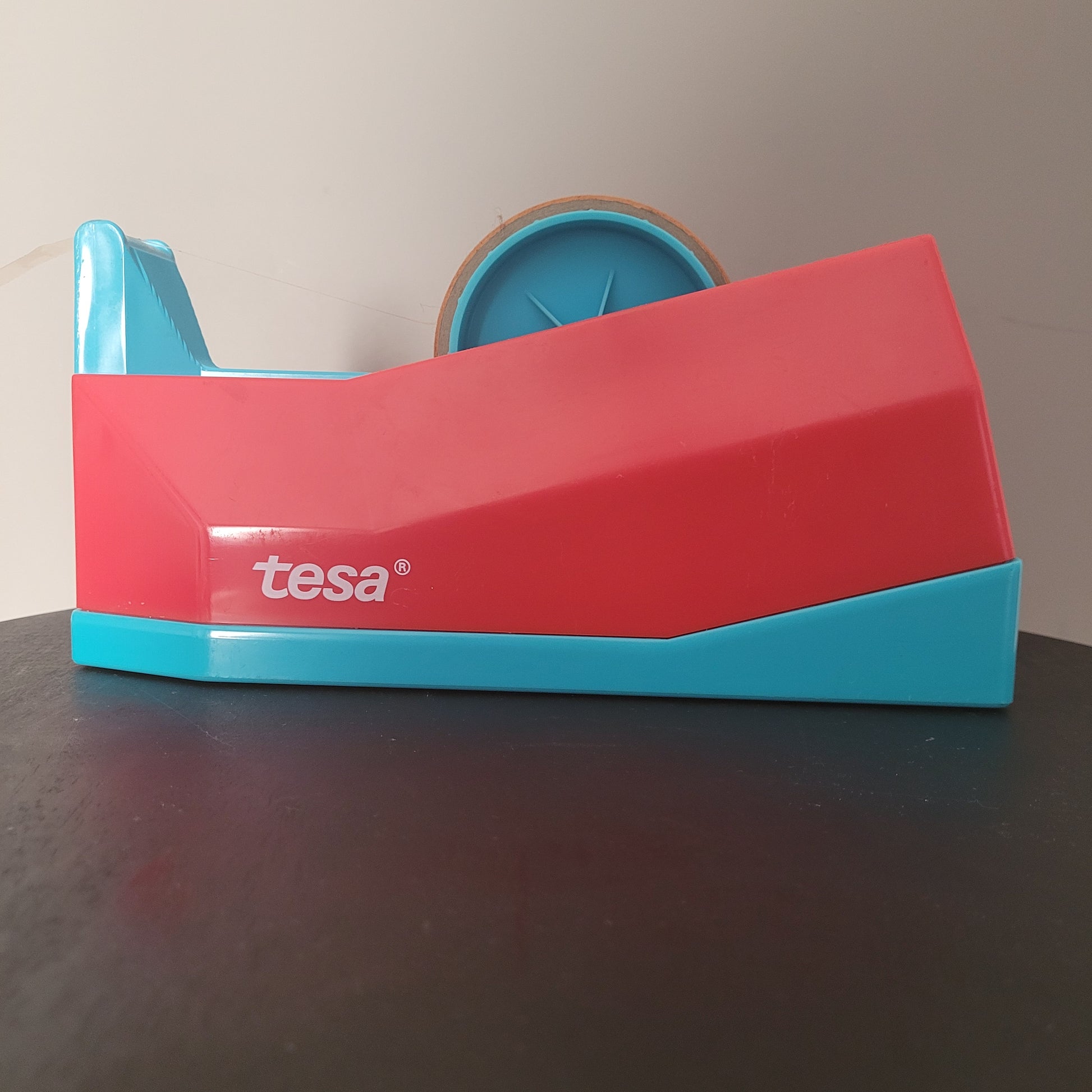 Tesa Abroller. Seitliche Aufnahme. Rot-blaues Gehäuse mit "tesa" - Aufschrift.