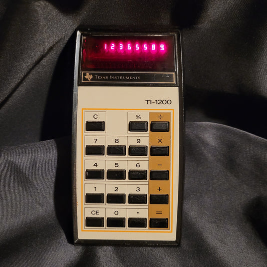 Vintage Texas Instruments TI-1200 Taschenrechner mit aktivierter, leuchtend roter LED-Anzeige und klassischem Tastenlayout.